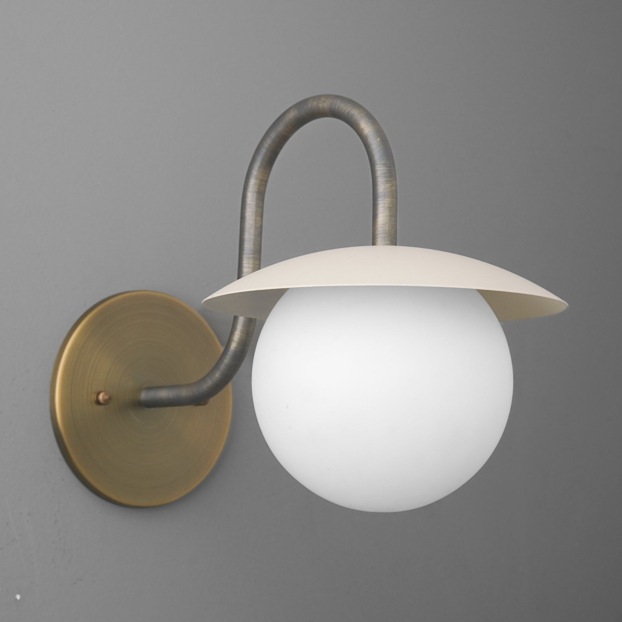 Wall sconce with curved antique brass arm and round white frosted glass globe shade topped with flat beige metal disc. - SCONCE MODEL NO. 2206