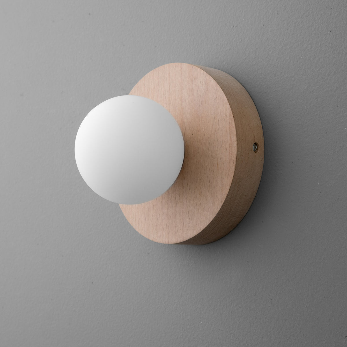 Minimalist wall sconce with matte white globe and round natural beechwood base on gray wall. - SCONCE MODEL NO. 4943