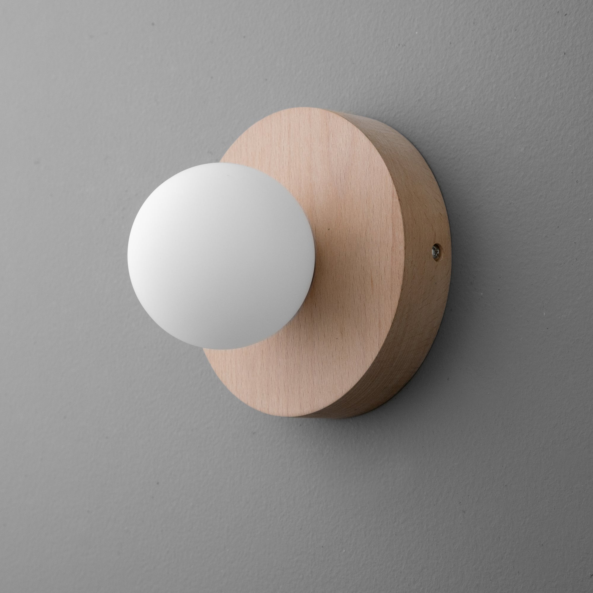Minimalist wall sconce with matte white globe and round natural beechwood base on gray wall. - SCONCE MODEL NO. 4943