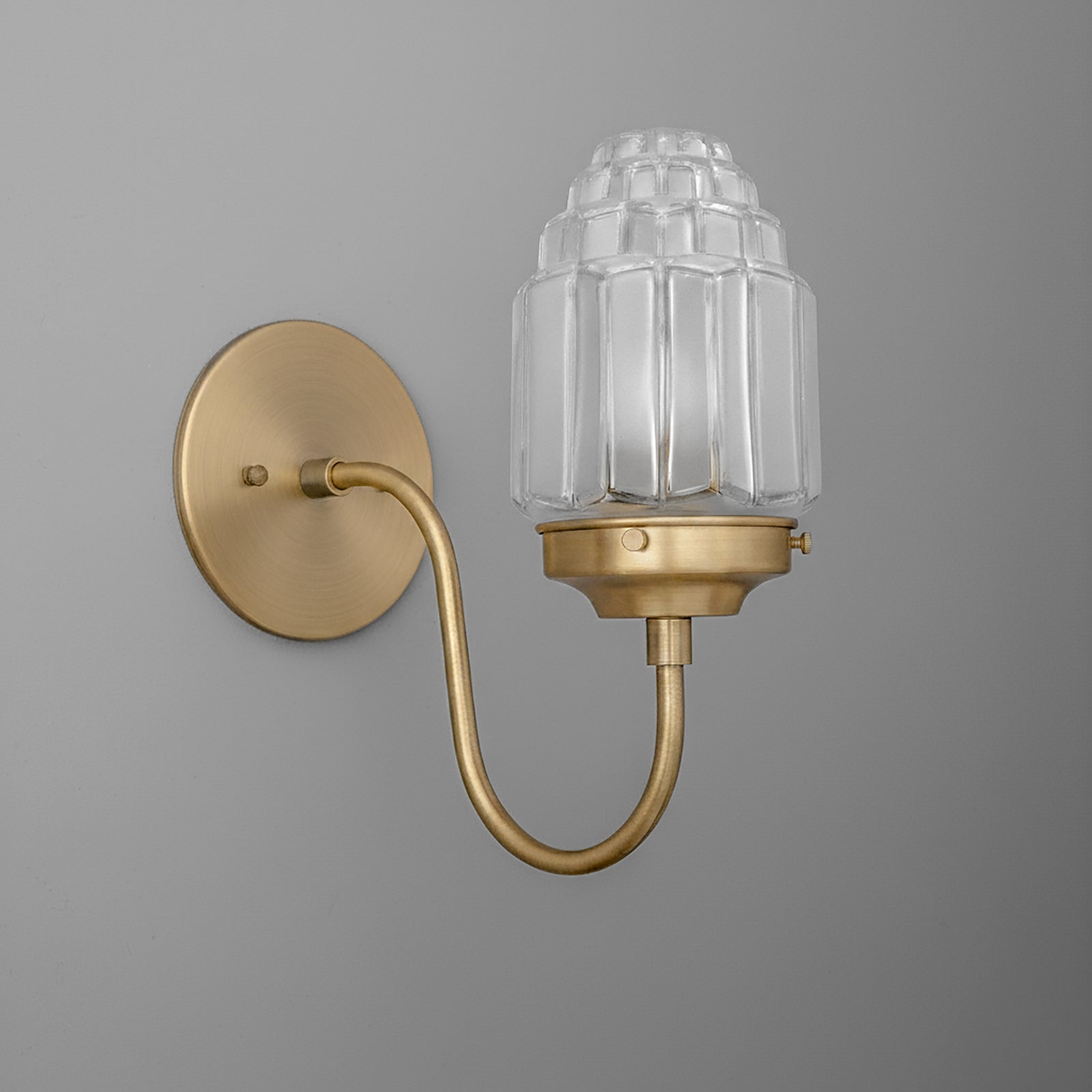 Wall sconce with a curved brass arm and clear ribbed glass shade in tiered design. - SCONCE MODEL NO. 1074
