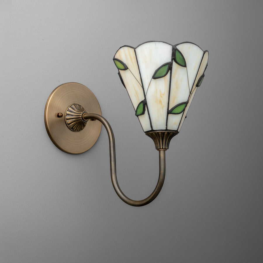 Antique brass wall sconce with curved arm and stained glass shade featuring green leaf accents. - SCONCE MODEL NO. 1053