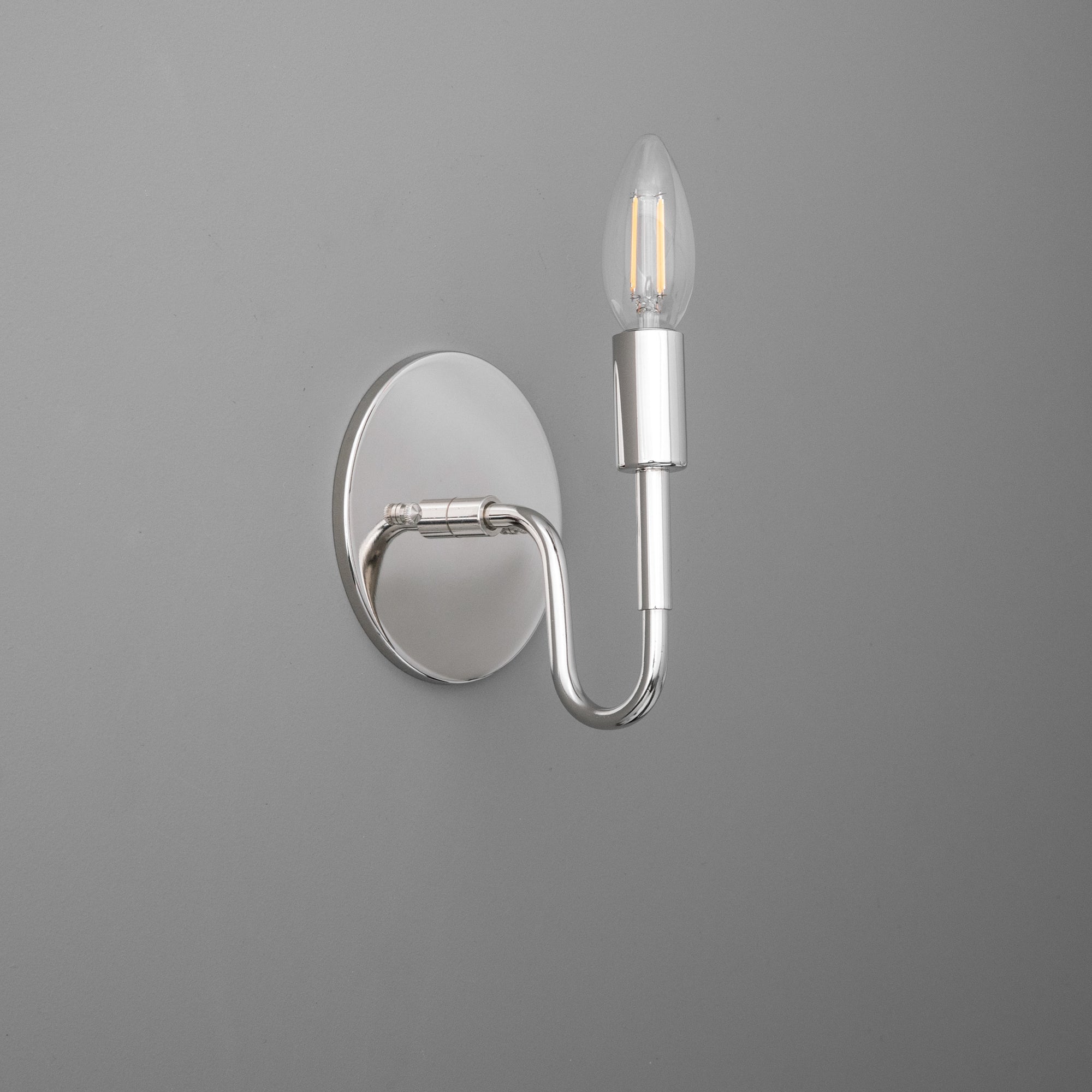 Chrome metal wall sconce with oval base and single curved arm holding a flame-shaped bulb. - SCONCE MODEL NO. 1100
