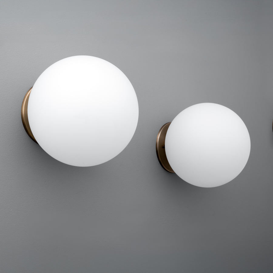 Two spherical white glass globe sconces with antique brass wall mounts on a gray background. - Sconce Model No. 5206