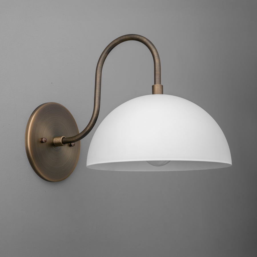 Wall sconce with antique brass curved arm and matte white dome shade against gray background. - SCONCE MODEL NO. 9092