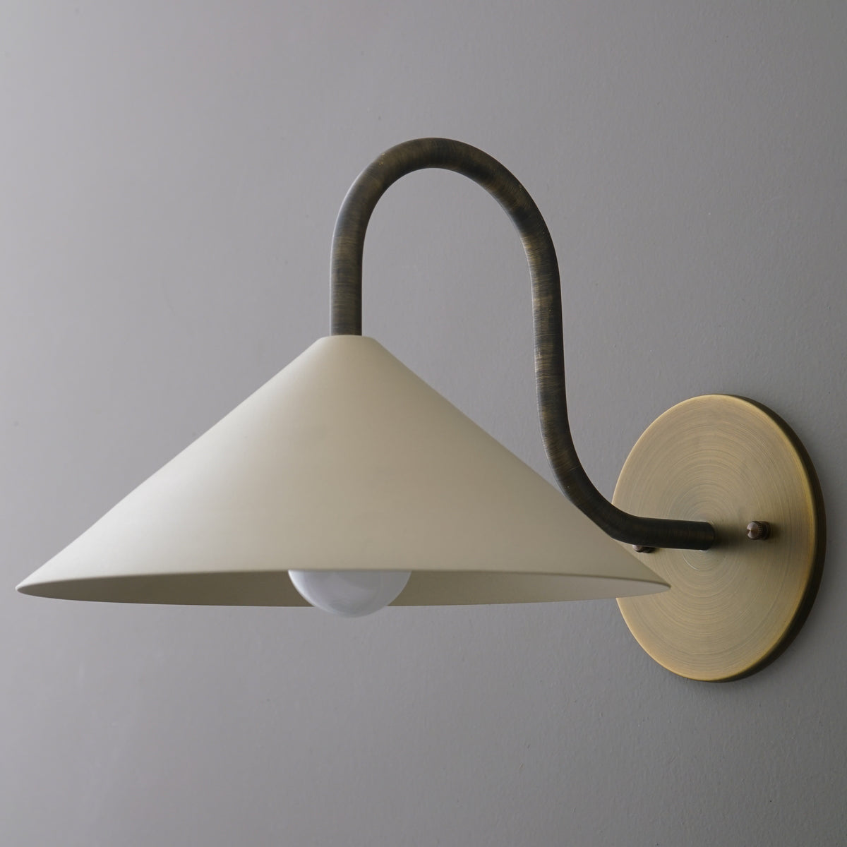 Wall sconce with matte white conical shade, curved dark metal arm, and round brass mounting plate. - SCONCE MODEL NO. 1015