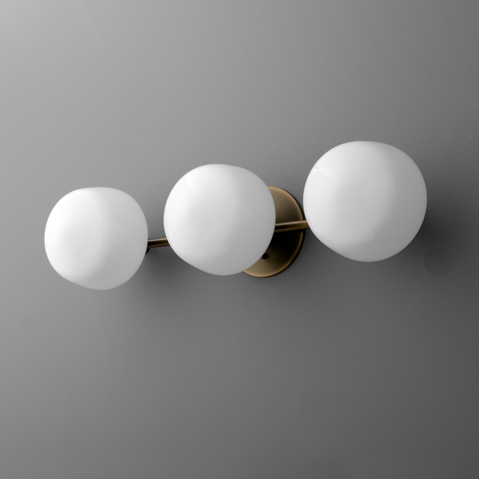 Three-bulb wall sconce with matte white glass globes and brass fixtures on a gray wall. - SCONCE MODEL NO. 1106