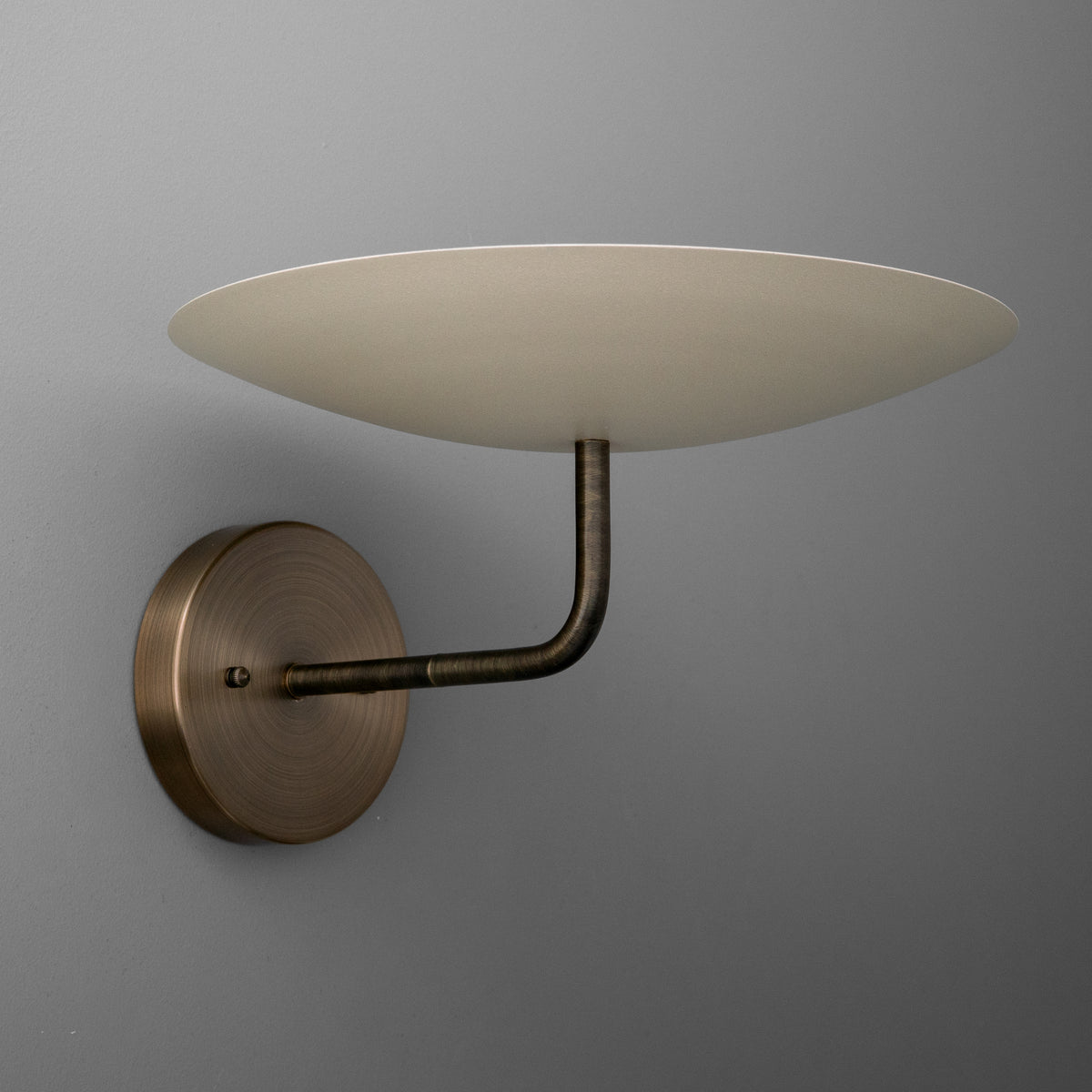 Wall-mounted sconce with round bronze base and curved arm supporting a wide, shallow beige lampshade. - SCONCE MODEL NO. 1504