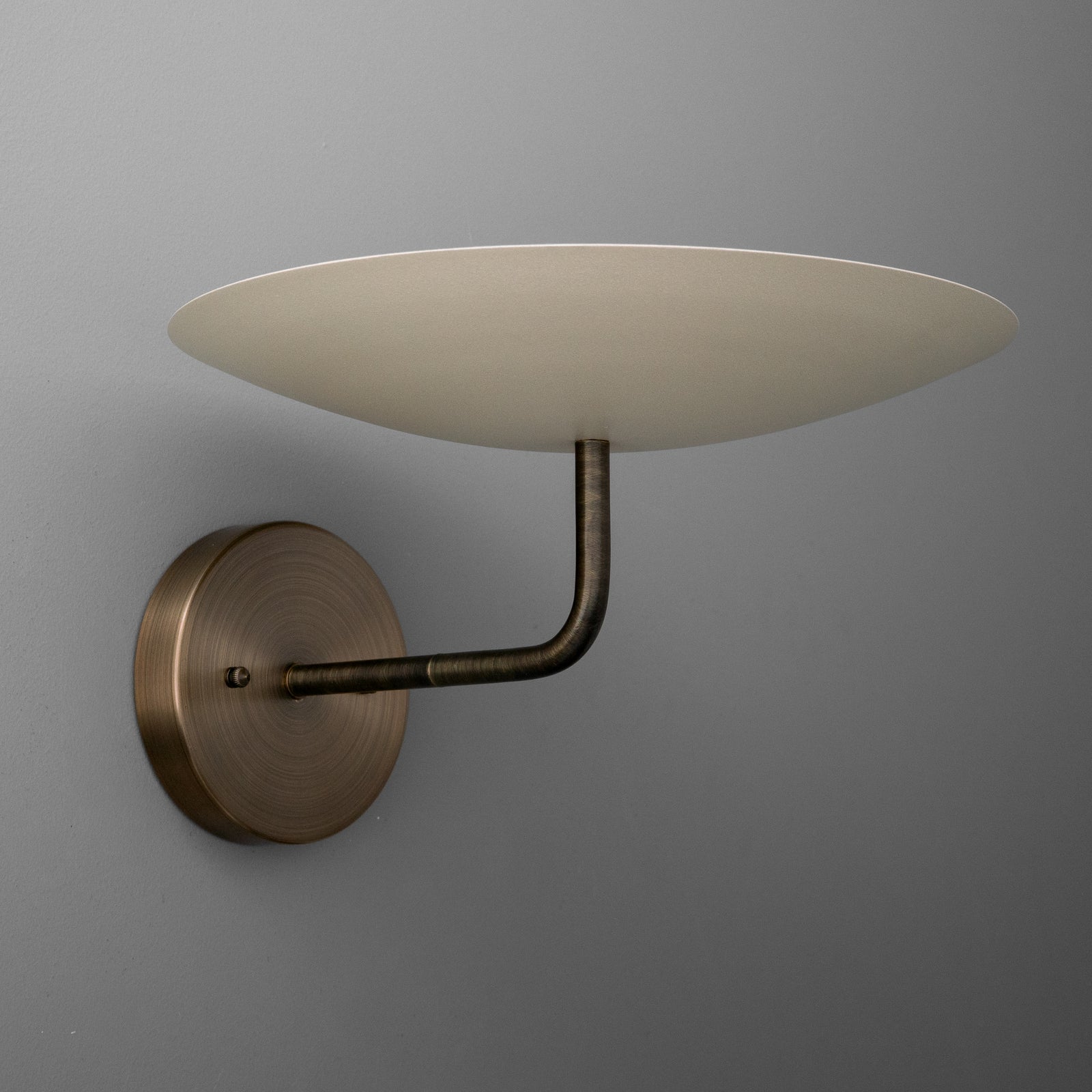 Wall-mounted sconce with round bronze base and curved arm supporting a wide, shallow beige lampshade. - SCONCE MODEL NO. 1504