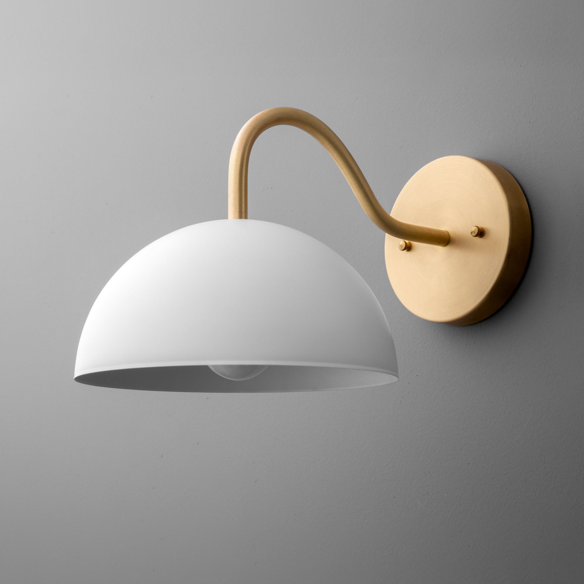 Wall sconce with a matte white dome shade and curved raw brass arm mounting on round brass base. - SCONCE MODEL NO. 6679