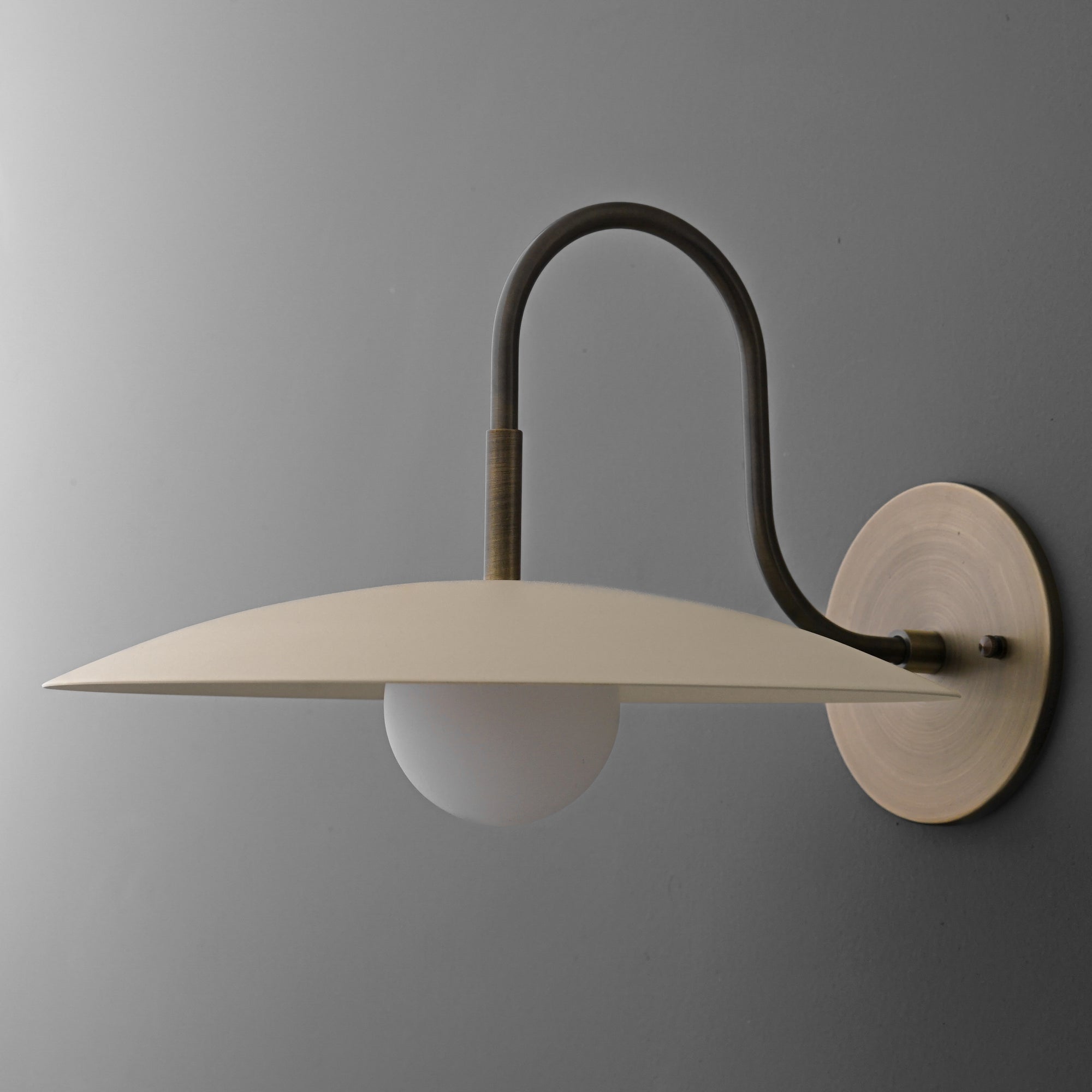 Wall sconce with matte cream disc shade and curved antique brass arm mounted on round base. - SCONCE MODEL NO. 9171