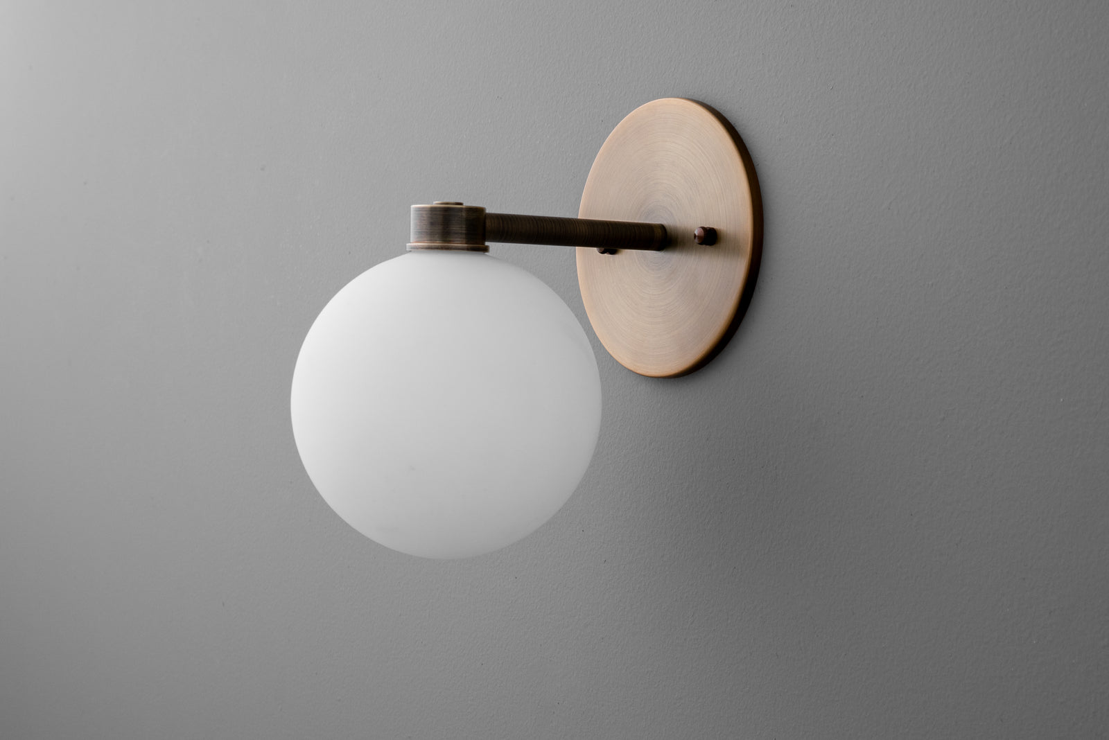 Minimalist wall sconce with frosted glass globe and antique brass finish on matte gray wall. - SCONCE MODEL NO. 2341