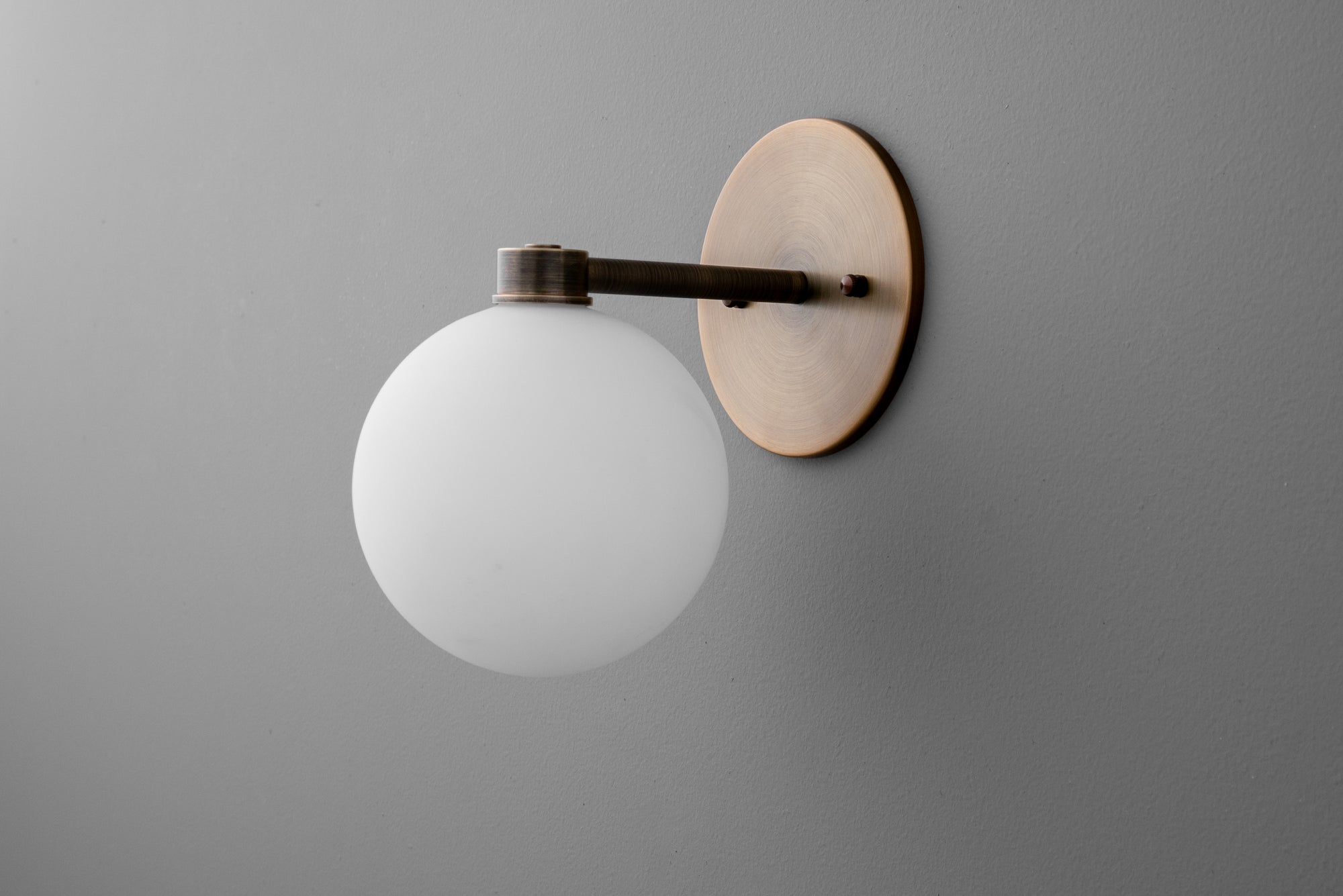 Minimalist wall sconce with frosted glass globe and antique brass finish on matte gray wall. - SCONCE MODEL NO. 2341