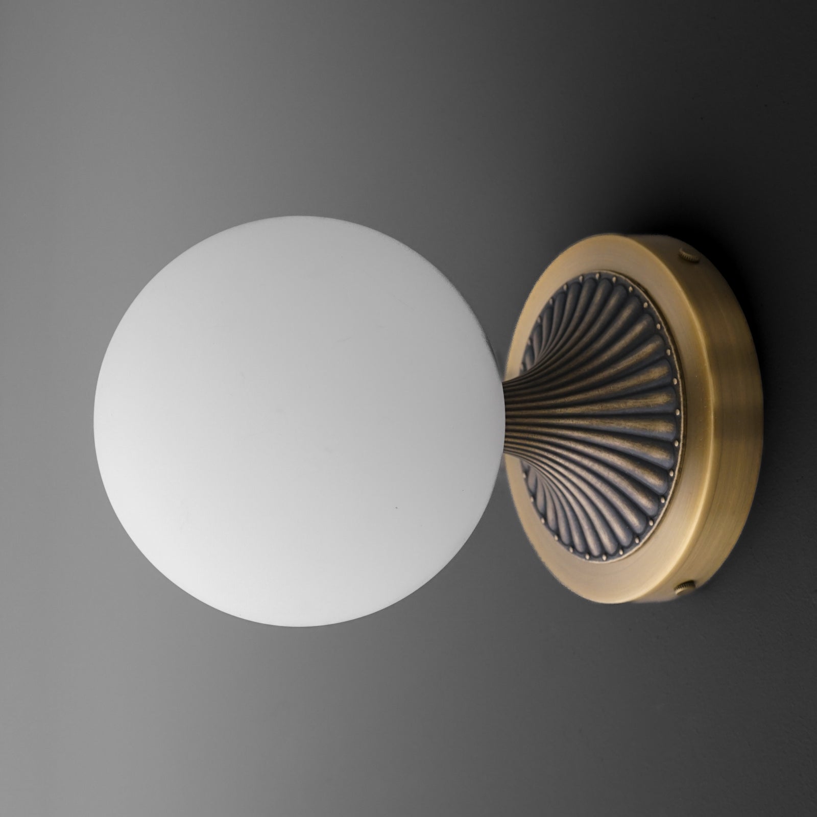 Wall-mounted sconce with a round frosted white glass globe and an antique brass base featuring radial black detailing. - SCONCE MODEL NO. 5363