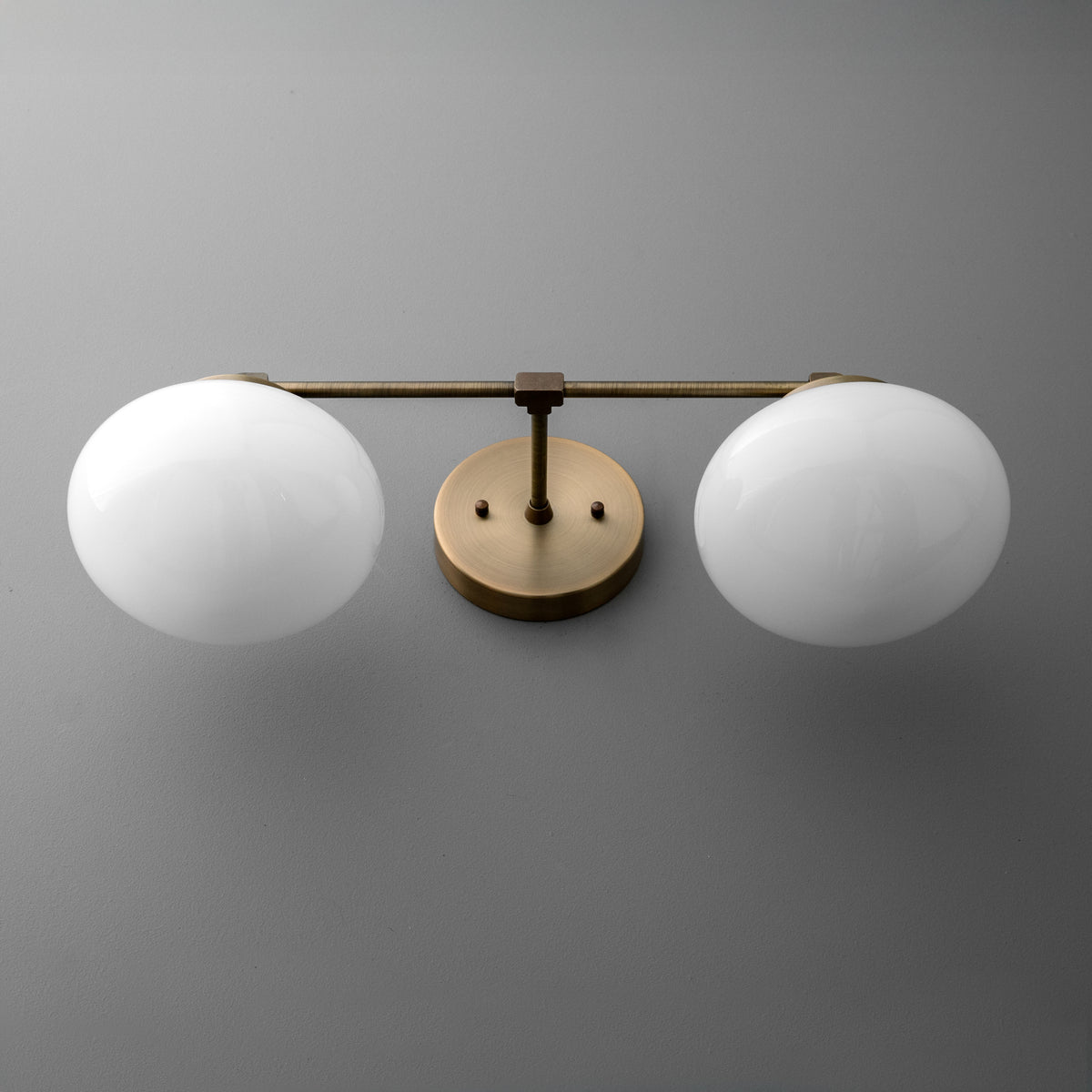 Two-bulb vanity light with round white glass shades and a brushed brass horizontal bar and wall mount. - VANITY LIGHT MODEL NO. 1167