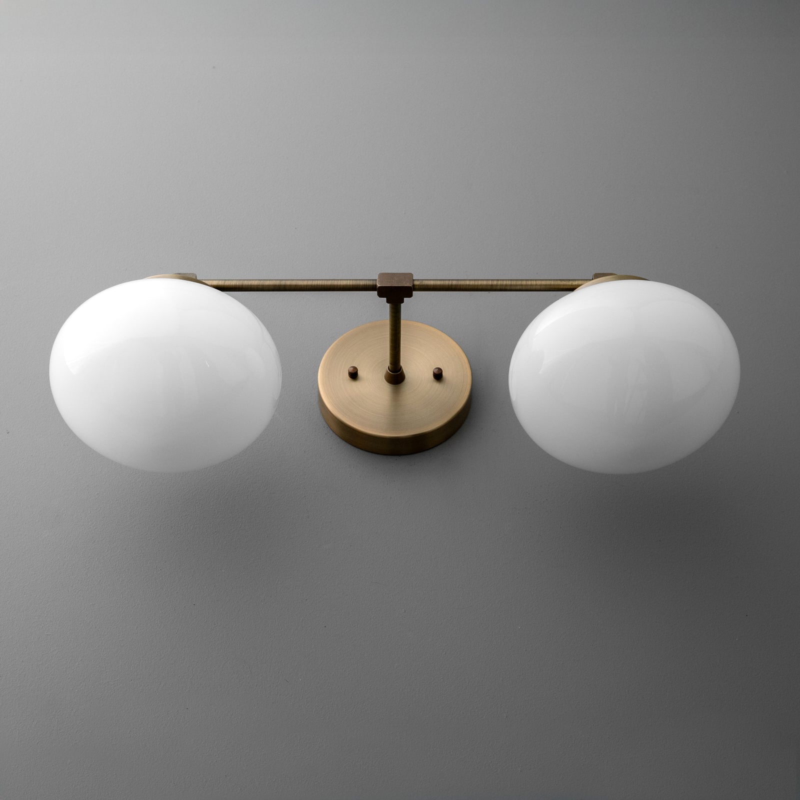 Two-bulb vanity light with round white glass shades and a brushed brass horizontal bar and wall mount. - VANITY LIGHT MODEL NO. 1167