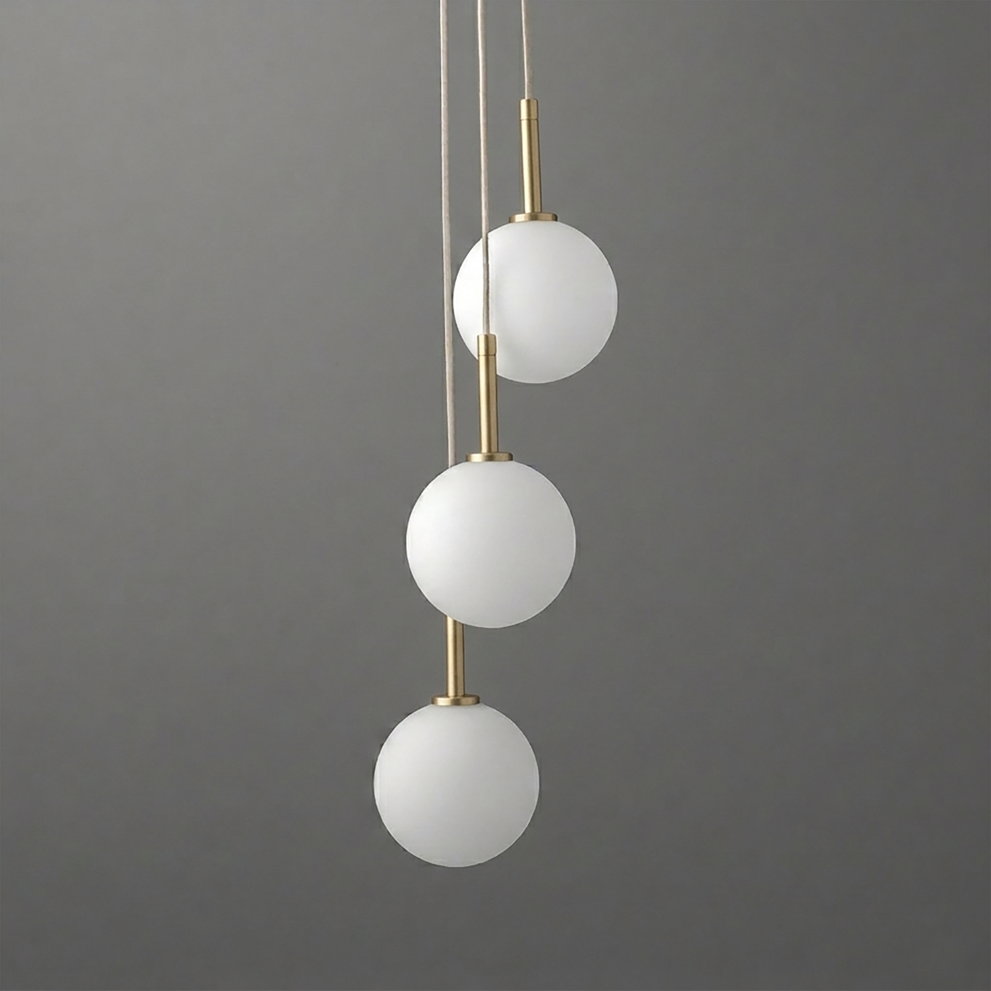 Modern chandelier with three white matte glass globes suspended vertically on slim brushed brass rods against a gray. - CHANDELIER MODEL NO. 4701