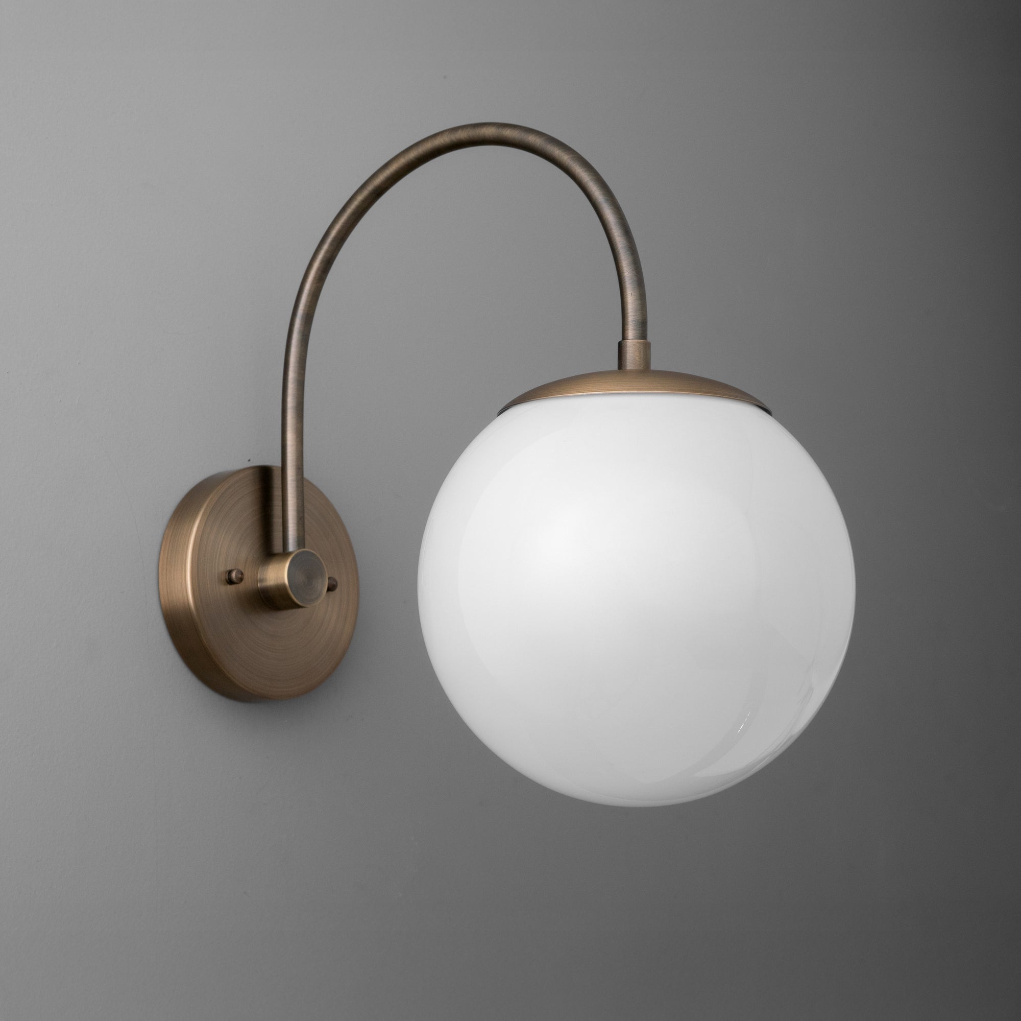 Wall sconce with antique brass finish featuring a curved arm and frosted white glass globe shade. - SCONCE MODEL NO. 2947
