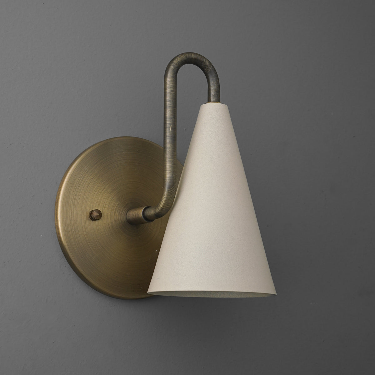 Sconce in Antique Brass with a looped arm holding a narrow cone shade, on a round wall plate. - SCONCE MODEL NO. 7485