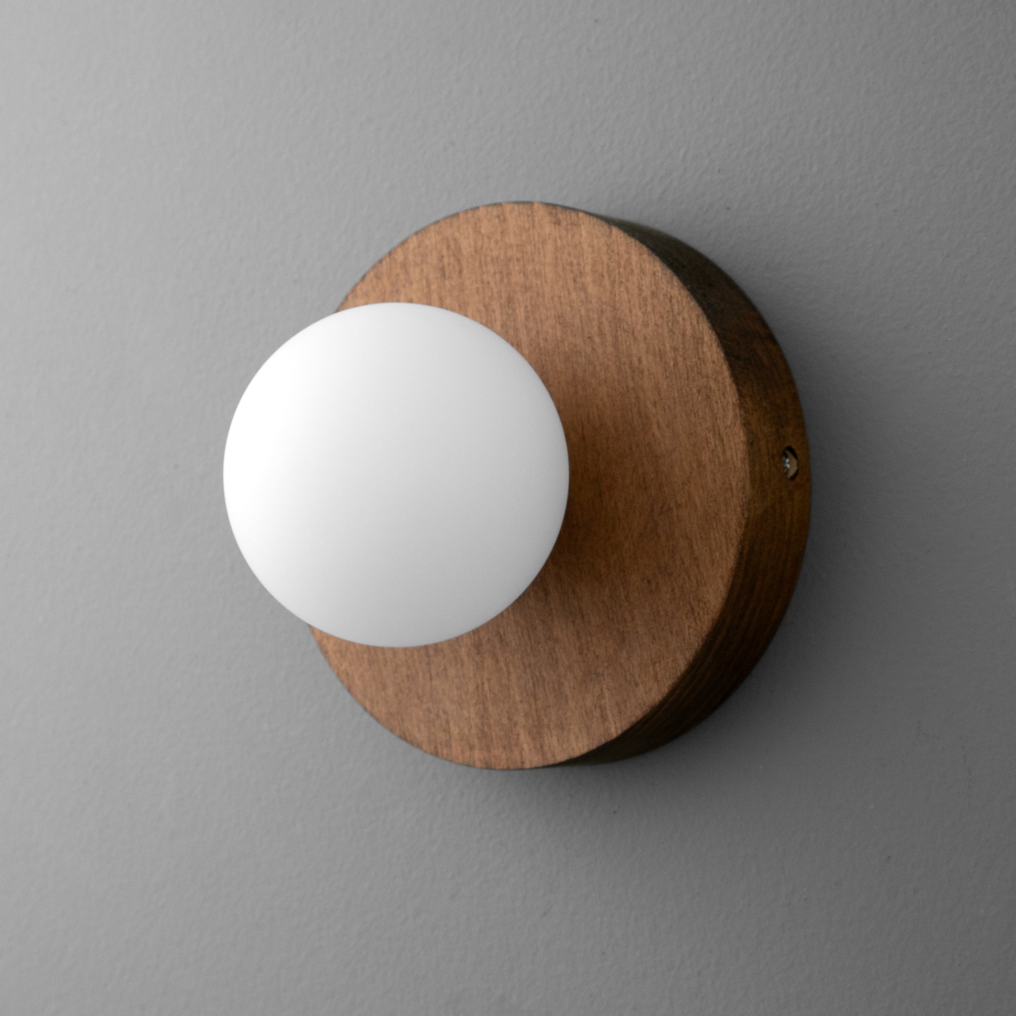 Wall sconce with round frosted white globe and circular oak-finish wooden base on gray wall. - SCONCE MODEL NO. 4943
