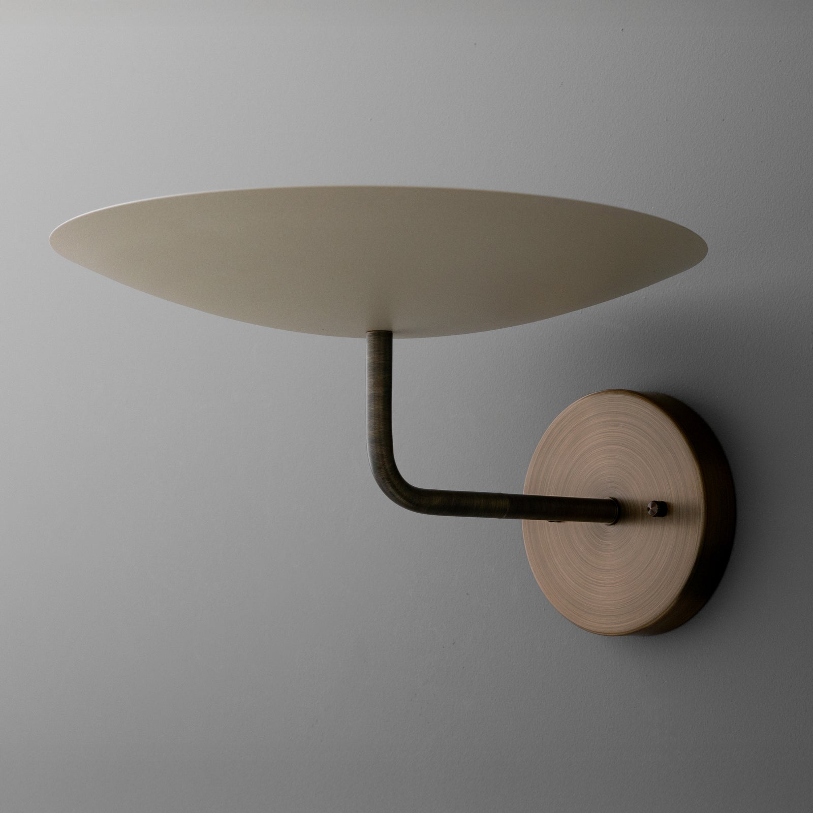 Wall-mounted sconce with round wooden base and flat, circular beige shade supported by a curved metal arm. - SCONCE MODEL NO. 1504