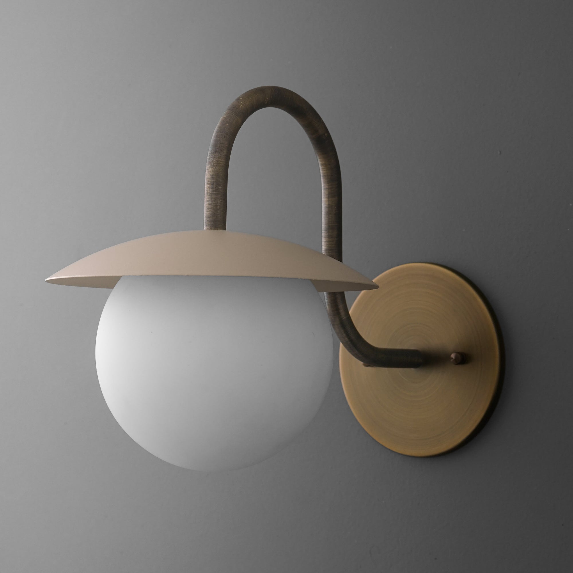 Modern wall sconce with frosted glass globe, curved dark metal arm, and flat brass shade and base plate. - SCONCE MODEL NO. 2206