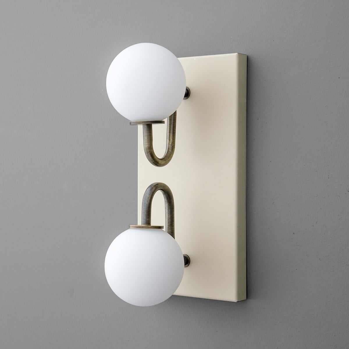 Wall sconce with two round white glass globes on aged brass curved metal arms and a rectangular cream backplate. - SCONCE MODEL NO. 9868