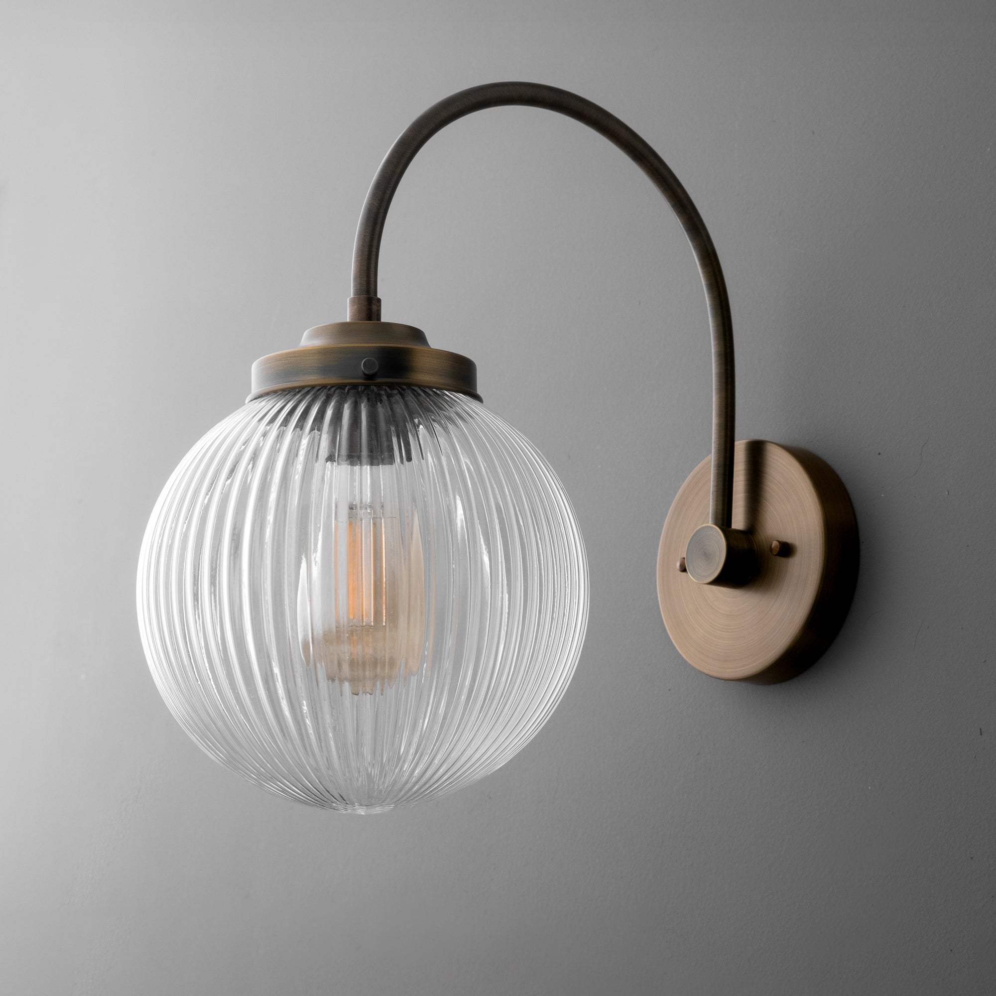 Wall sconce with ribbed clear glass globe and curved antique brass arm mounted on round backplate. - SCONCE MODEL NO. 8763