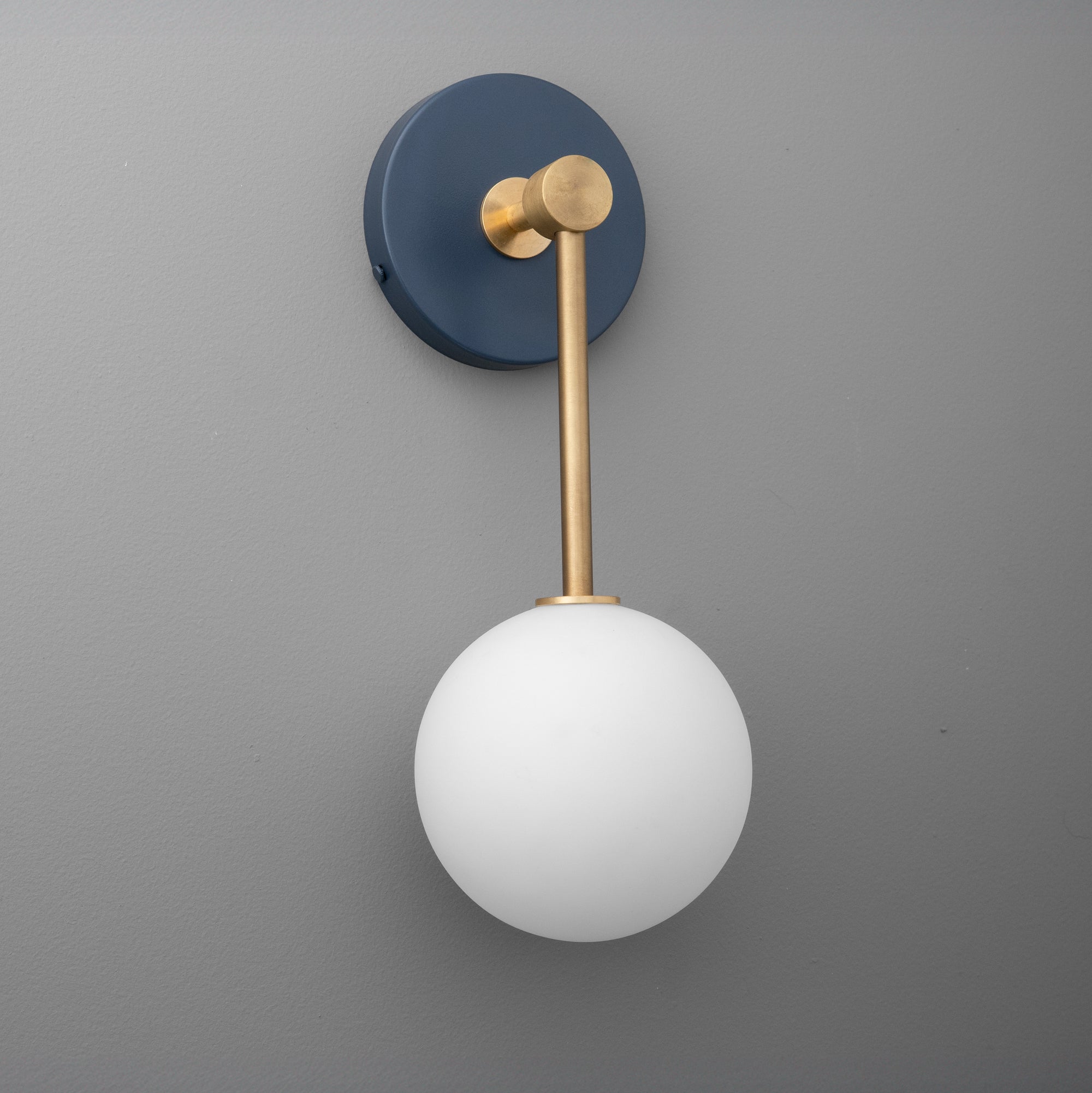Wall sconce with raw brass arm, coal blue round backplate, and white frosted glass globe shade. - Sconce Model No. 5999