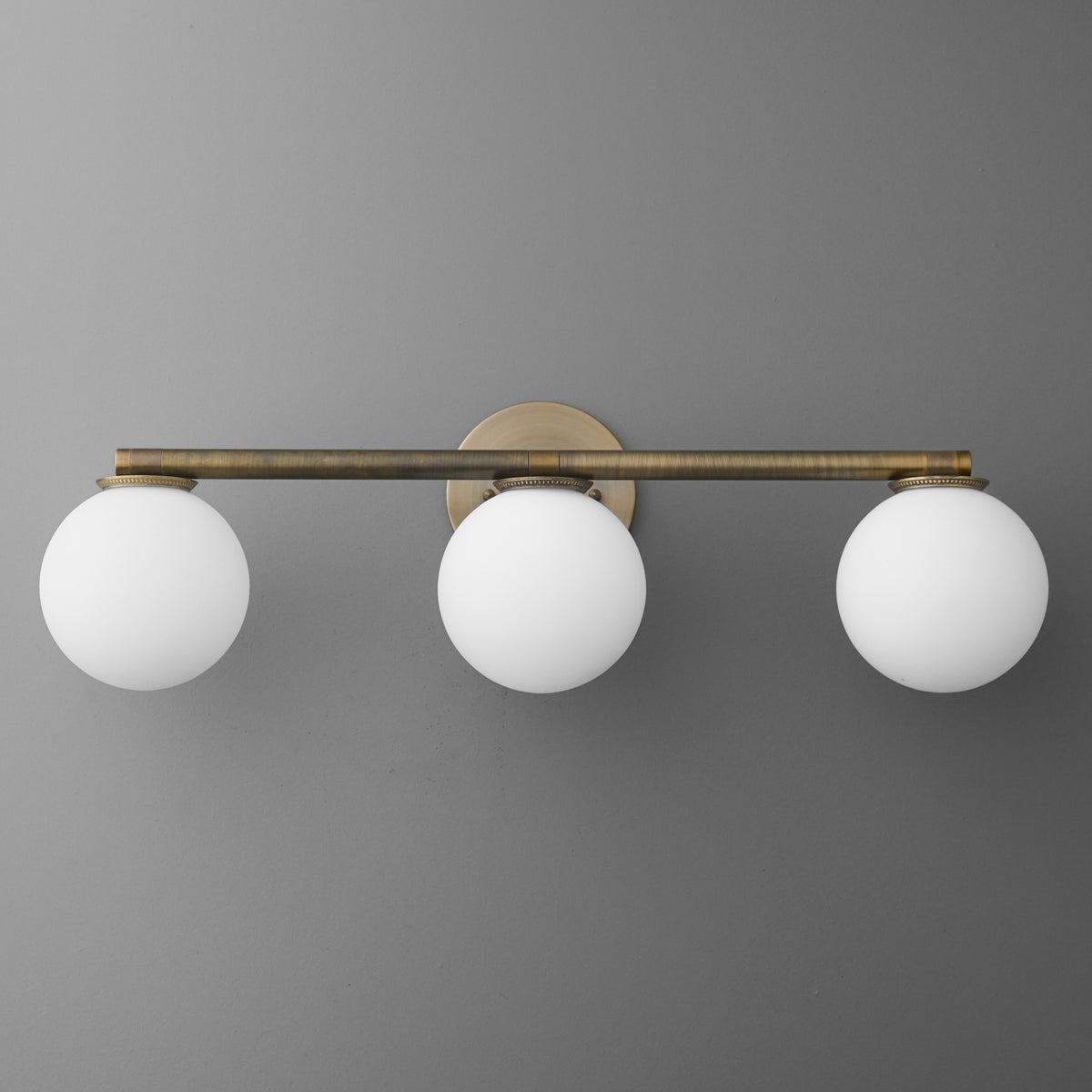 Three-bulb vanity light with round white glass shades and antique brass horizontal bar mount. - VANITY LIGHT MODEL NO. 1158