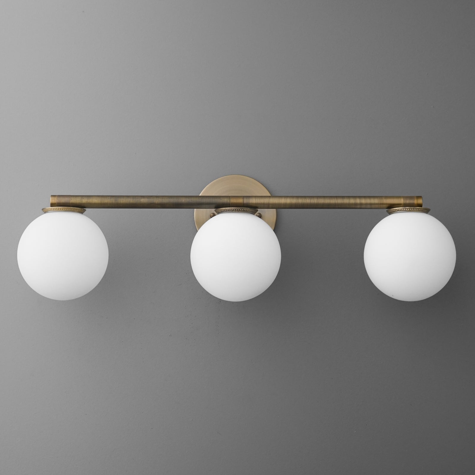Three-bulb vanity light with round white glass shades and antique brass horizontal bar mount. - VANITY LIGHT MODEL NO. 1158