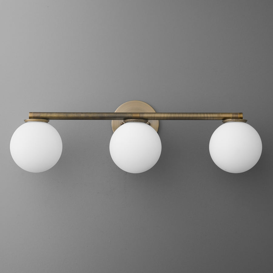 Three-bulb vanity light with round white glass shades and antique brass horizontal bar mount. - VANITY LIGHT MODEL NO. 1158