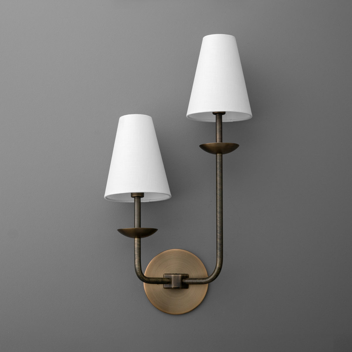 Two-light sconce in Antique Brass, Long Arm Right, with tapered linen empire shades on bobeches rising from a round wall plate. - SCONCE MODEL NO. 1966