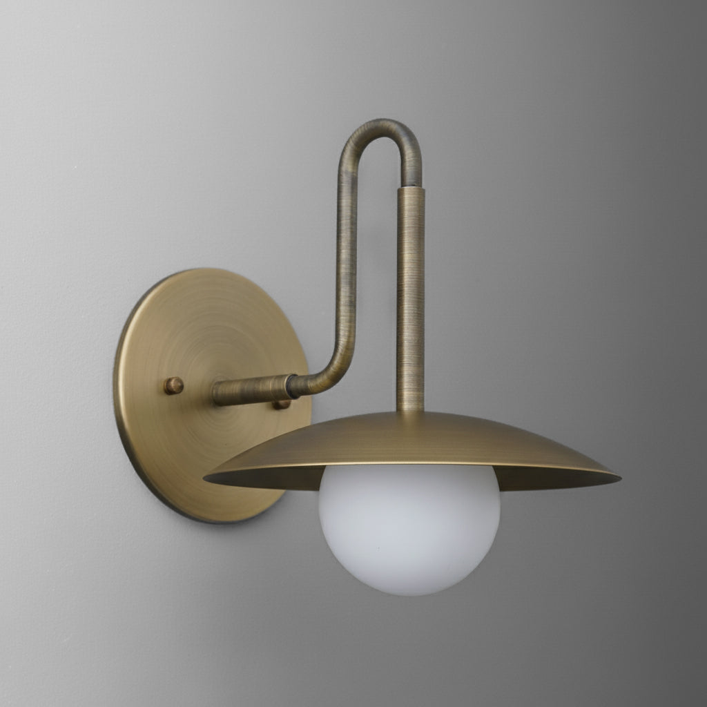Antique brass single-bulb wall sconce with curved arm and flat circular shade over frosted globe bulb. - SCONCE MODEL NO. 1013