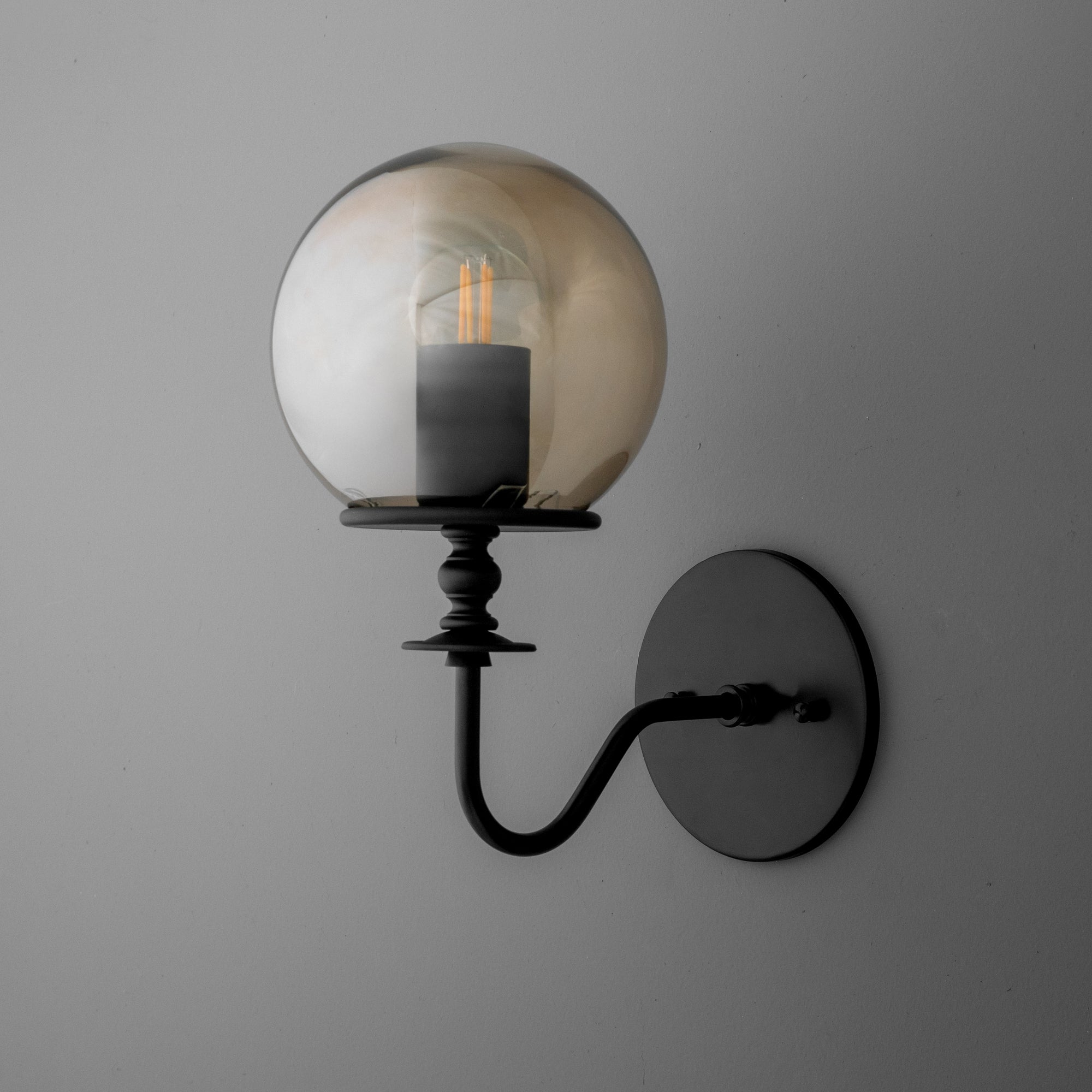 Matte black metal wall sconce with curved arm and clear glass globe shade enclosing filament bulb. - SCONCE MODEL NO. 1029