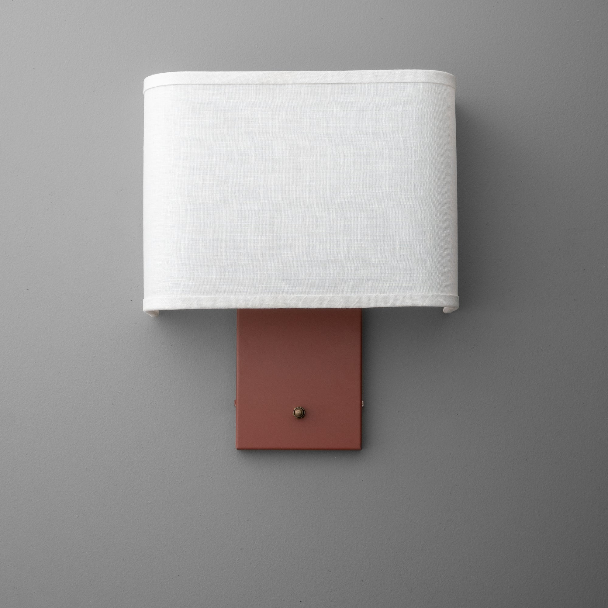 Wall sconce with white fabric shade and rectangular muted brick red metal base with small brass rotary switch. - SCONCE MODEL NO. 7769