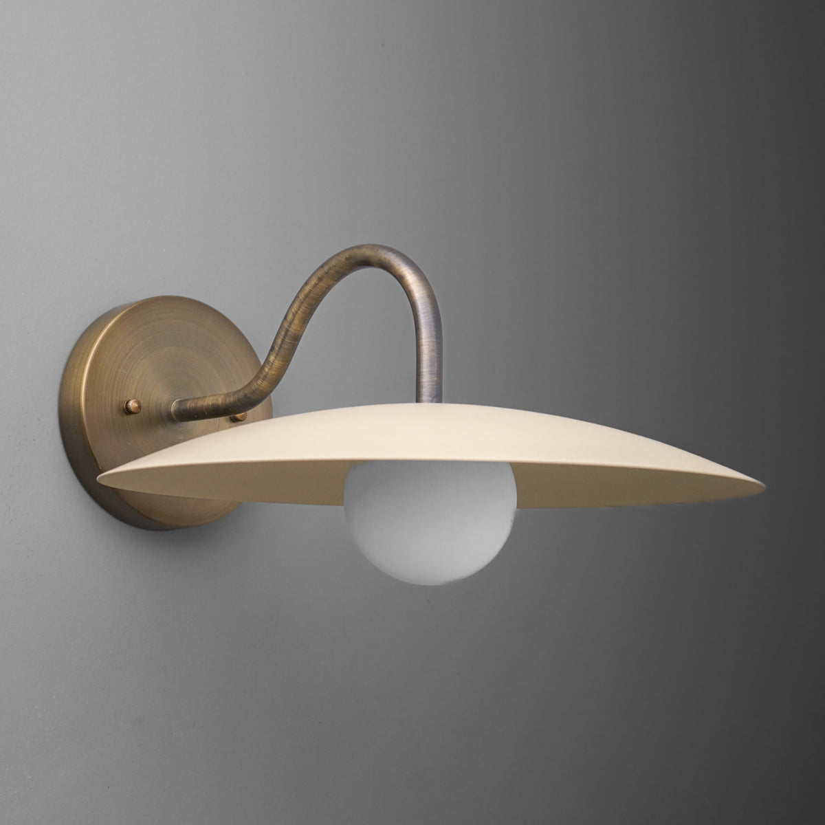 Antique brass wall sconce with curved arm and flat cream lampshade over round bulb. - SCONCE MODEL NO. 2162