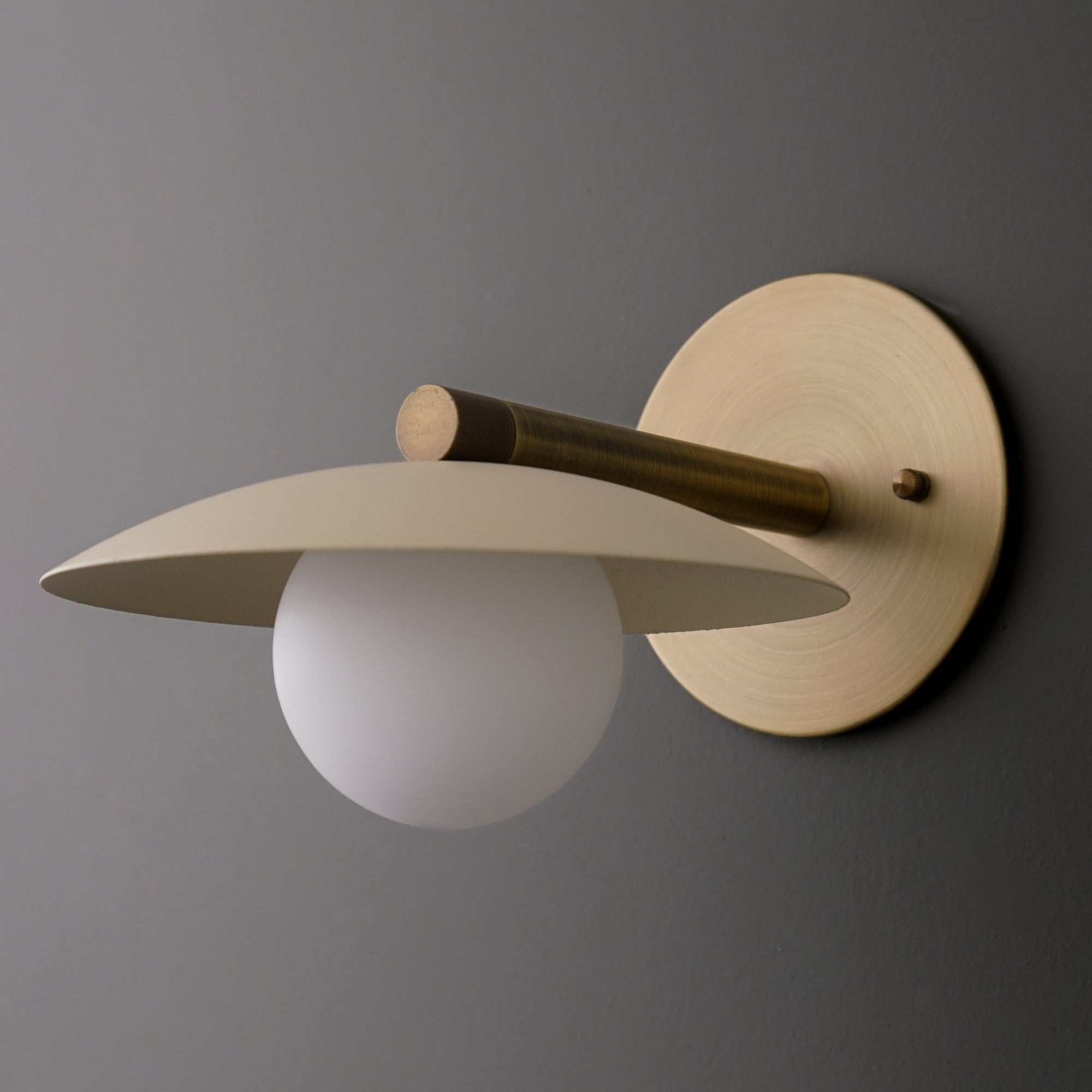 Antique brass sconce with cream flat metal shade and frosted globe bulb on round wall plate. - SCONCE MODEL NO. 9875