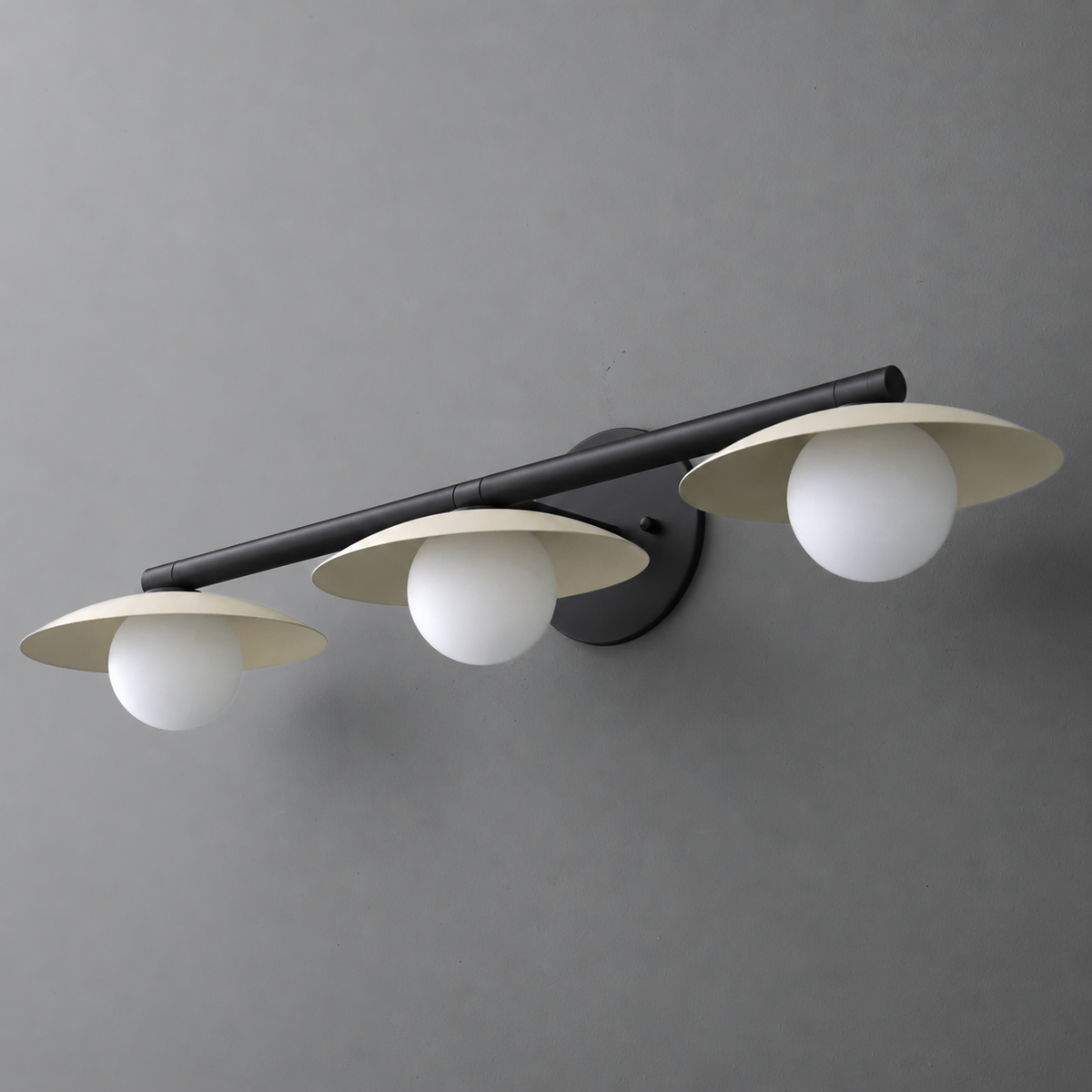 Black metal vanity light with three white globe bulbs and wide flat shades mounted on a horizontal bar. - VANITY LIGHT MODEL NO. 1156