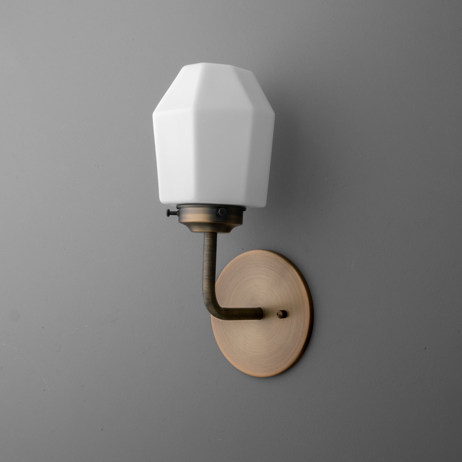 Wall sconce with matte brass round base and angled black arm holding a white geometric glass shade. - SCONCE MODEL NO. 1062