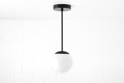 Mid-century modern pendant light with a black metal fixture and a white frosted glass globe shade. - PENDANT MODEL NO. 7056