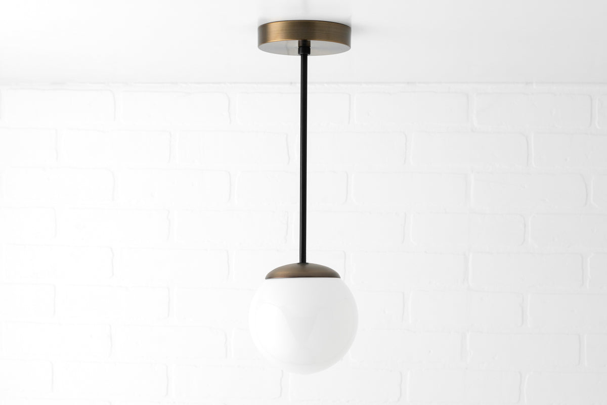 Mid-century pendant light with white glass globe and black rod suspended from brass ceiling mount. - PENDANT MODEL NO. 7056