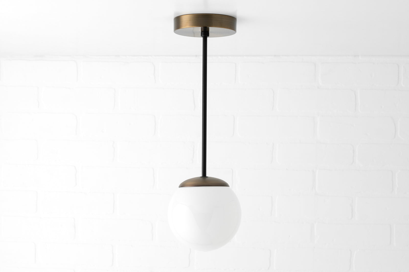 Mid-century pendant light with white glass globe and black rod suspended from brass ceiling mount. - PENDANT MODEL NO. 7056
