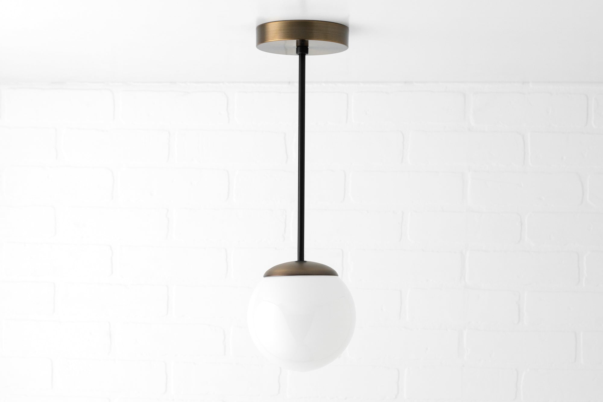 Mid-century pendant light with white glass globe and black rod suspended from brass ceiling mount. - PENDANT MODEL NO. 7056