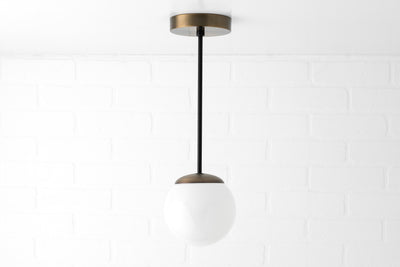 Mid-century pendant light with white glass globe and black rod suspended from brass ceiling mount. - PENDANT MODEL NO. 7056