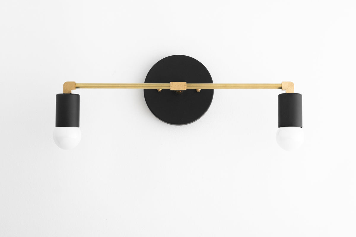 Two-light vanity light in Black/R. Brass/Black, with a Black wall plate and sockets on a Raw Brass bar. - VANITY LIGHT MODEL NO. 8412