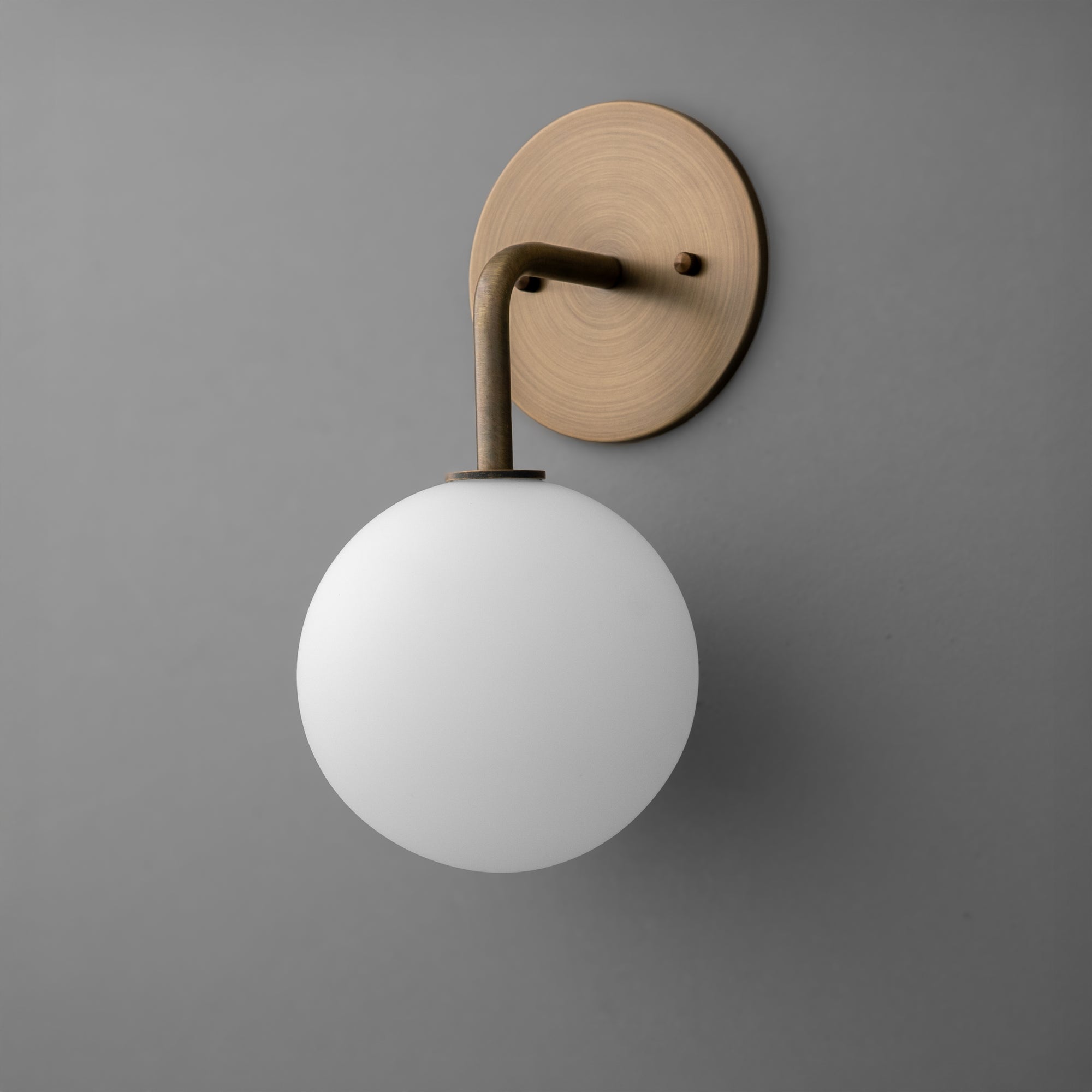 Minimal wall sconce with matte white glass globe and antique brass round backplate and arm. - SCONCE MODEL NO. 7660
