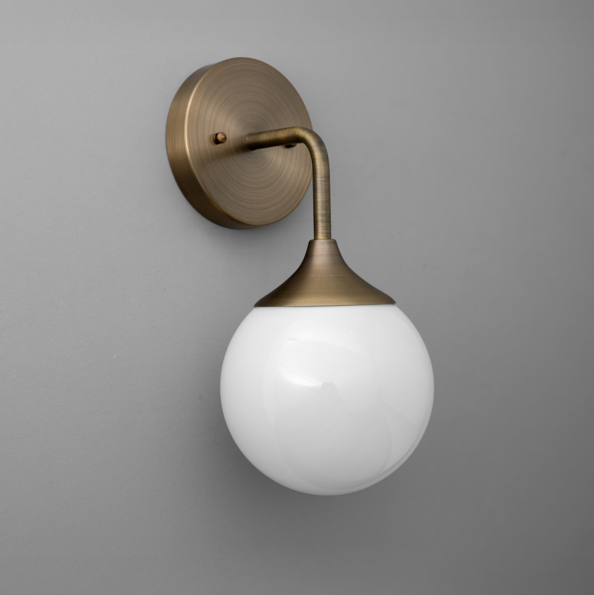 Antique brass wall sconce with curved arm and white frosted glass globe shade on gray background. - SCONCE MODEL NO. 1752