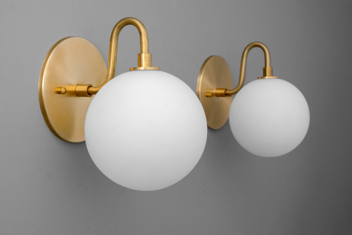 Pair of antique brass wall sconces with white frosted glass globe shades mounted on round backplates. - SCONCE MODEL NO. 8637