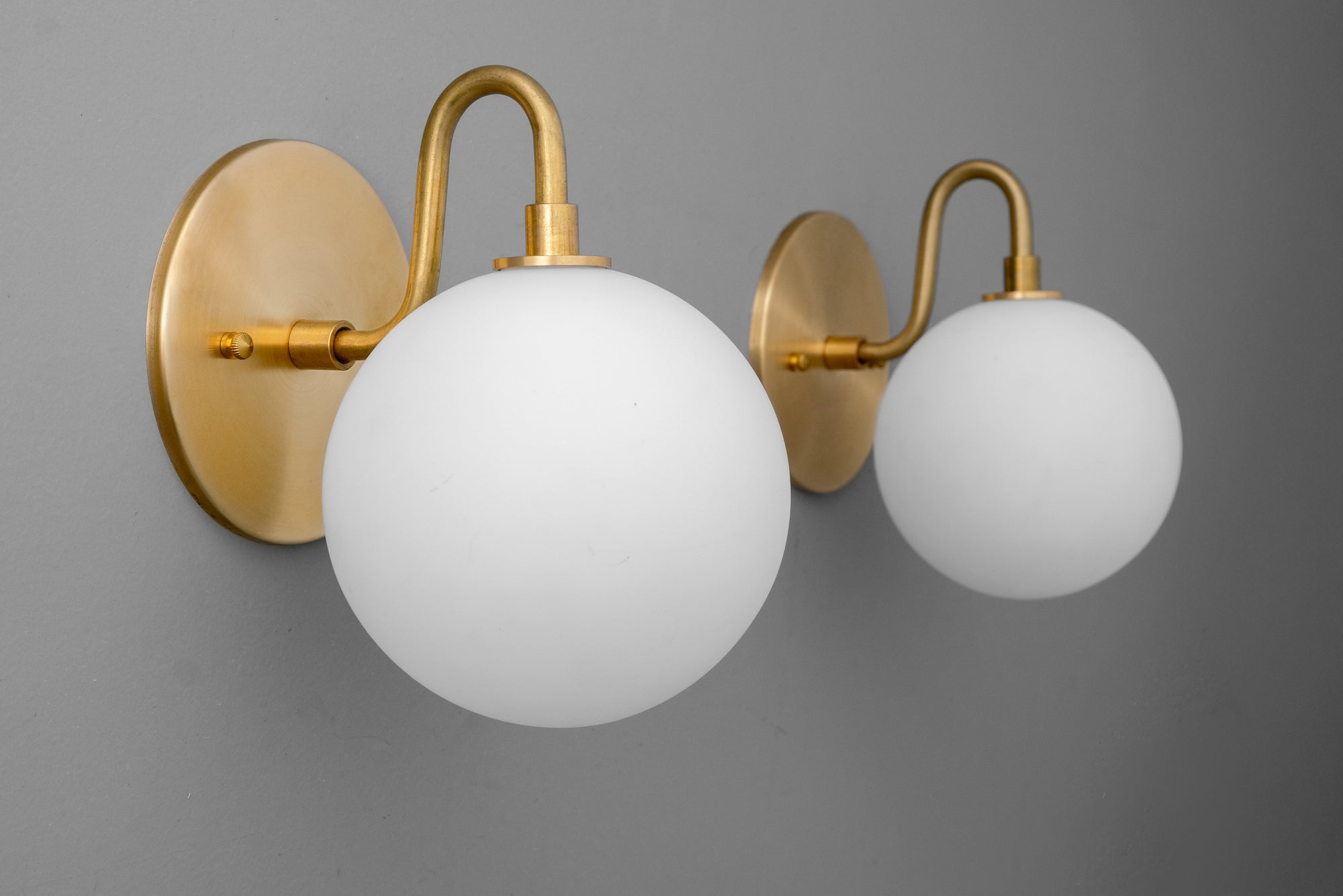 Pair of antique brass wall sconces with white frosted glass globe shades mounted on round backplates. - SCONCE MODEL NO. 8637