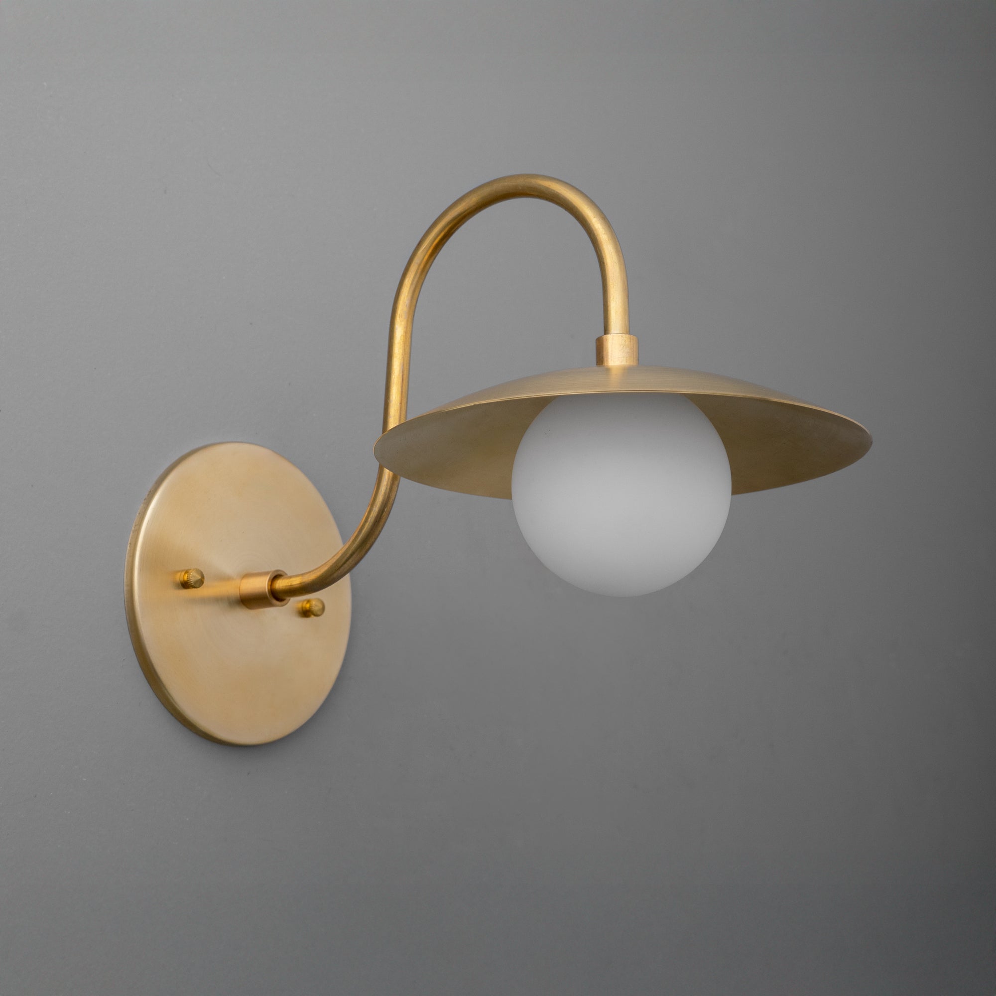 Antique brass wall sconce with curved arm and frosted globe shade against gray background. - SCONCE MODEL NO. 3799